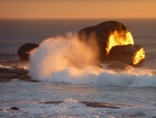 A wave breaking on sunlit rocks at sunset